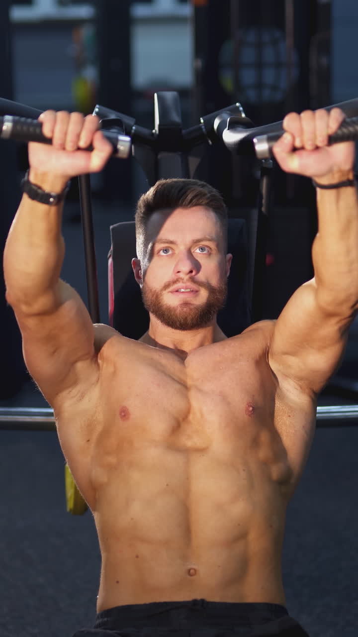 Muscular handsome man working hard in the gym. Bodybuilder with naked torso doing exercise. Vertical video