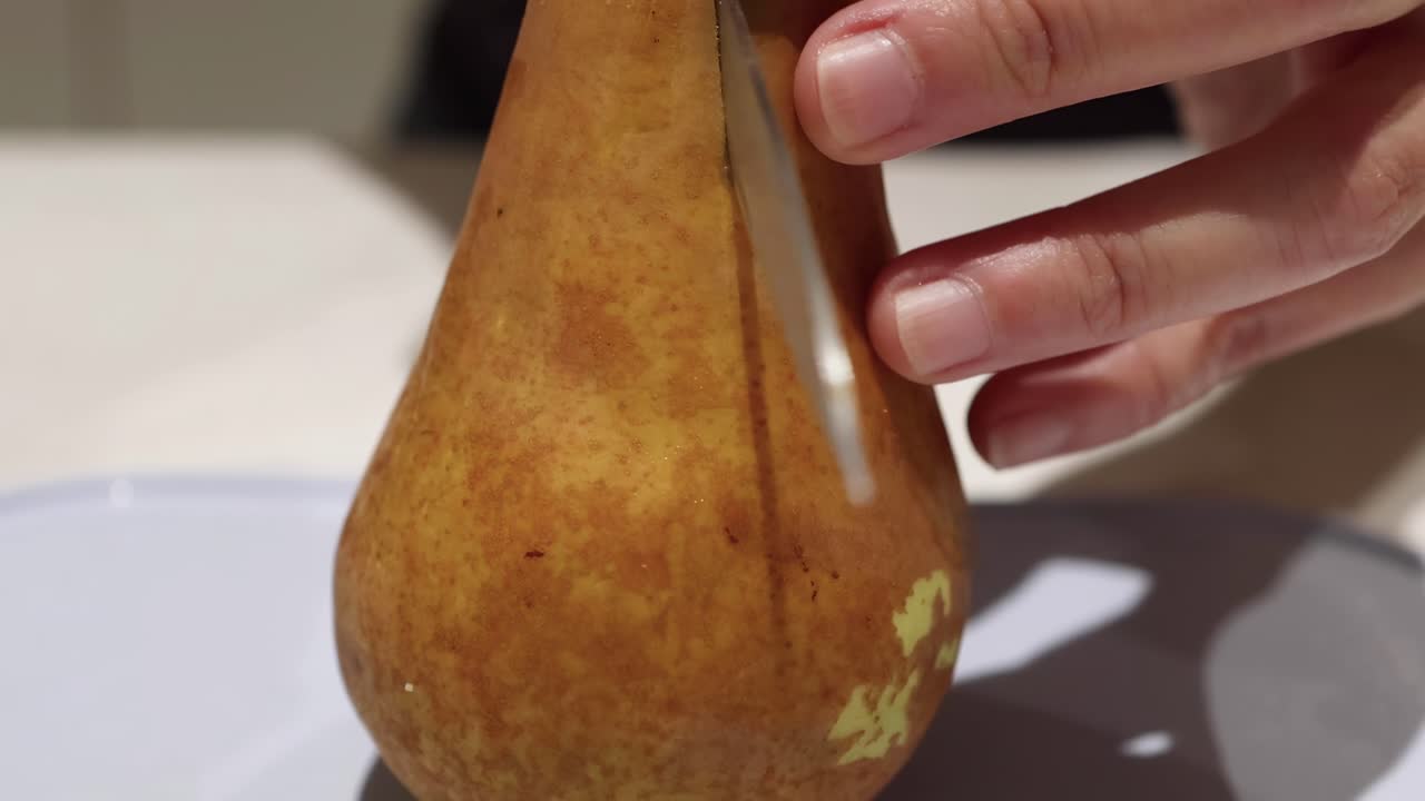 Close-up sequence of a hand slicing a pear with a knife on a white plate.
