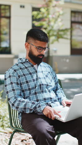 Indischer-Freiberufler,-Der-Online-Arbeitet-Und-Mit-Dem-Laptop-Auf-Der-Straße-In-Der-Stadt-Auf-Der-Website-Surft