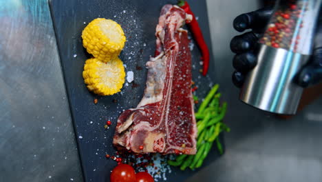 covering a piece of meat with salt and pepper. beef with vegetables on the charcuterie board. close up. vertical view.