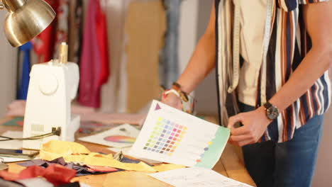 Focused-biracial-male-fashion-designer-sketching-design-standing-at-desk-in-studio,-slow-motion