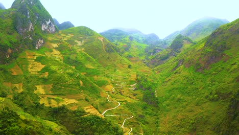 aerial dolly forward of a winding road cut into the mountainside of the misty mountains of ma pi leng pass in northern vietnam