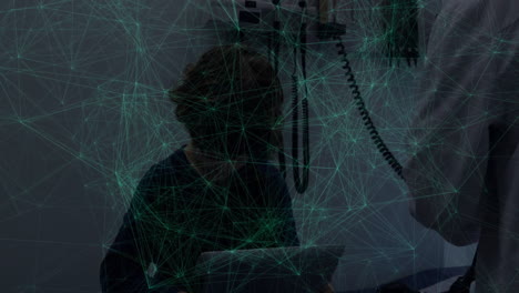 Male doctor using stethoscope on seated boy holding tablet in clinic, showing network overlay
