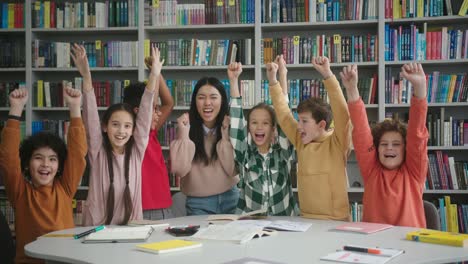 happy teacher and schoolchildren put hands up in library