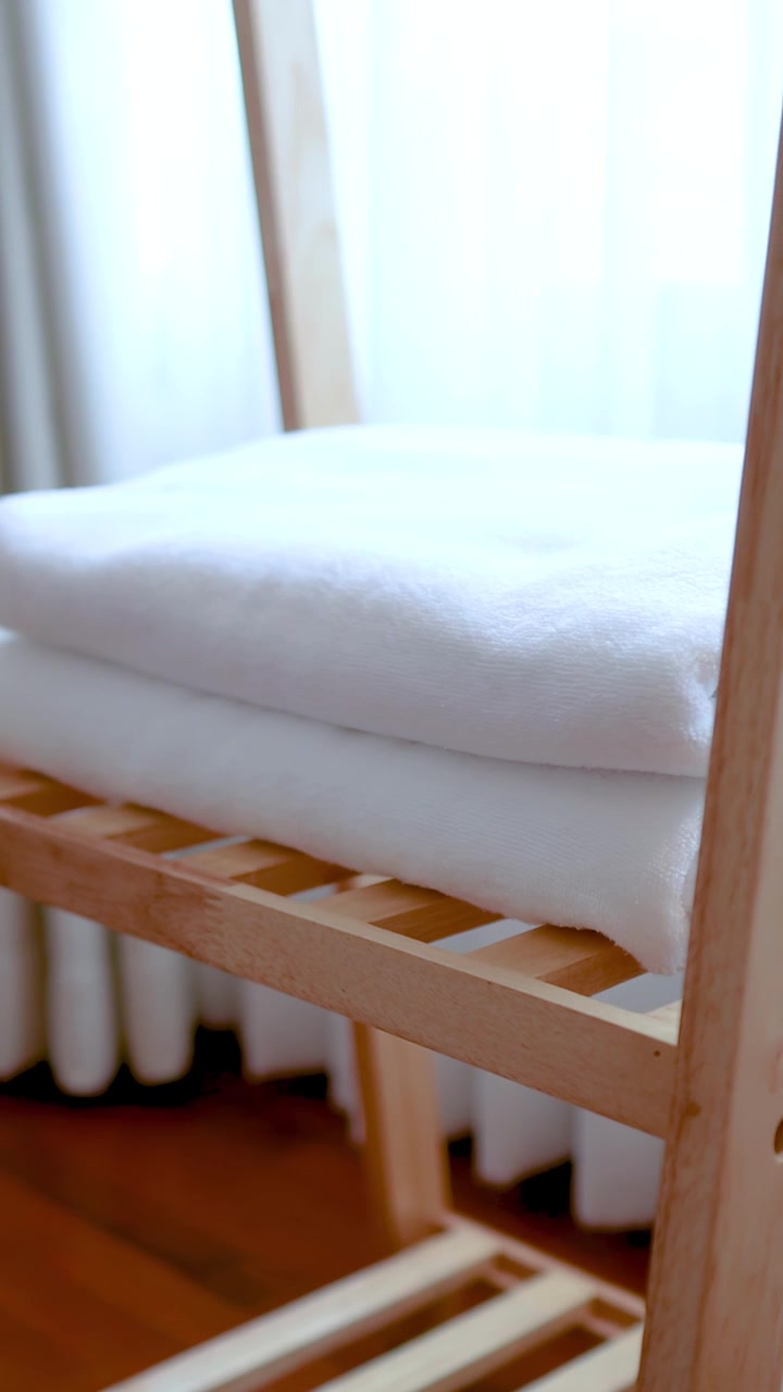 Close-up of hands organizing fresh white towels on a wooden shelf in bright lighting.