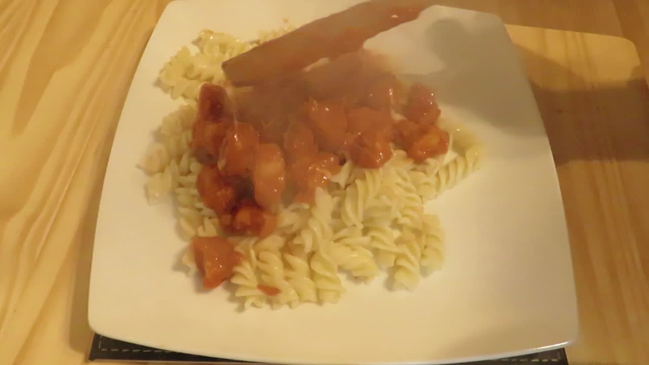 Adding ready made red sauce with chicken onto pasta, adding graded cheese on top and readying a plate for serving of pasta with chicken recipe