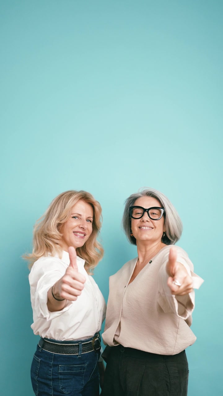 Two Mature Women Giving Thumbs Up Against a Teal Background