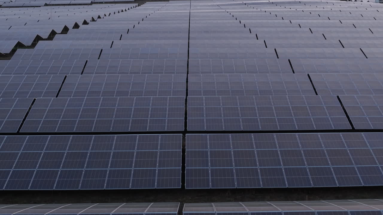 Cinematic drone shot of a large solar panel farm captured during sunset in rural Bulgaria. The golden light reflects over the photovoltaic array, highlighting modern renewable energy infrastructure.