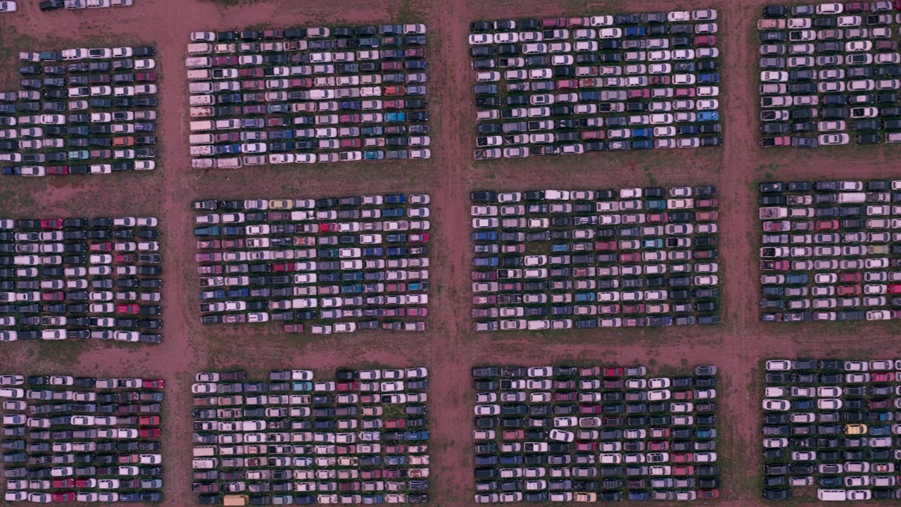 Panoramique aérien zénithal vers la droite au-dessus de blocs géométriques de véhicules stationnés disposés en rangées denses dans un grand centre de stockage automobile