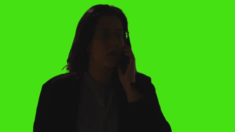 silhouette of woman talking on mobile phone against green screen background with low key lighting