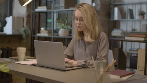 Serious-Blonde-Female-Employee-Working-On-Laptop-Computer-In-The-Office