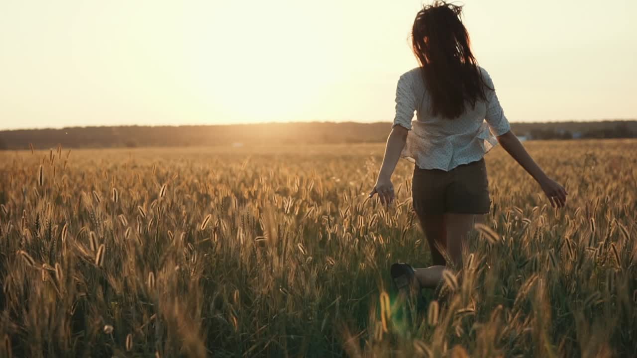 mujer caminando por un campo de trigo al atardecer