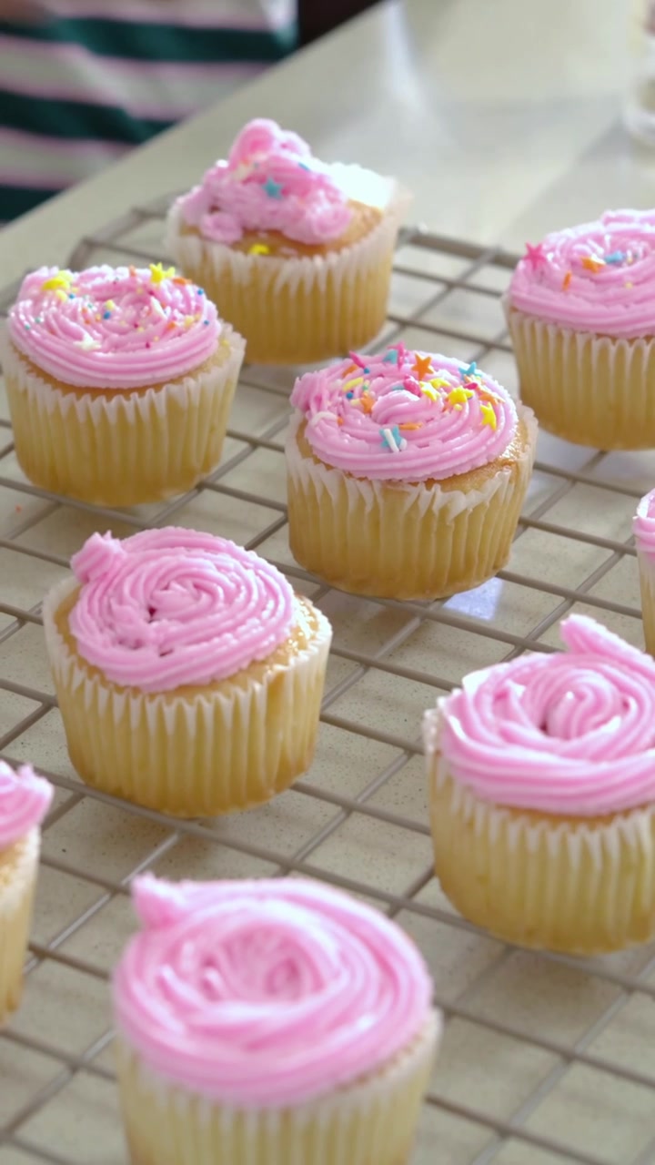 Vídeo vertical: Avó alcançando para colocar granulado em cupcakes em casa enquanto menina de listras ajuda.