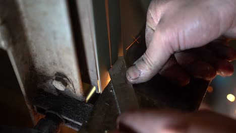 sanding belt used to grind metal part for creating metal blade making sparks, close up handheld shot