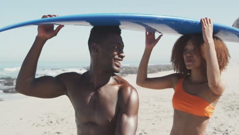 african american couple holding a surfboard on their heads