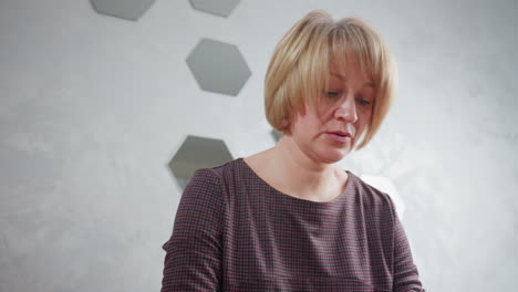 middle-aged woman in checkered dress focused on task, standing near a wall decorated with geometric mirrors, soft lighting creating a calm ambiance in a modern interior setting