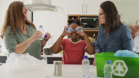 Happy-caucasian-lesbian-couple-and-their-african-american-daughter-sorting-waste-in-kitchen