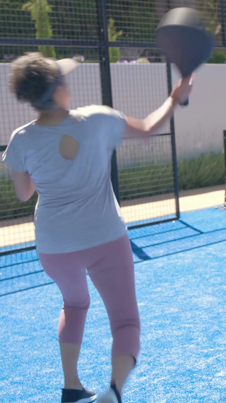 Vertical video: Reacting to shot, woman in grey top and pink leggings swinging paddle on blue court
