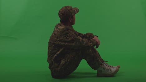 full body of asian male soldier looking around then touching his head being sad due to the war while sitting on the floor on green screen background