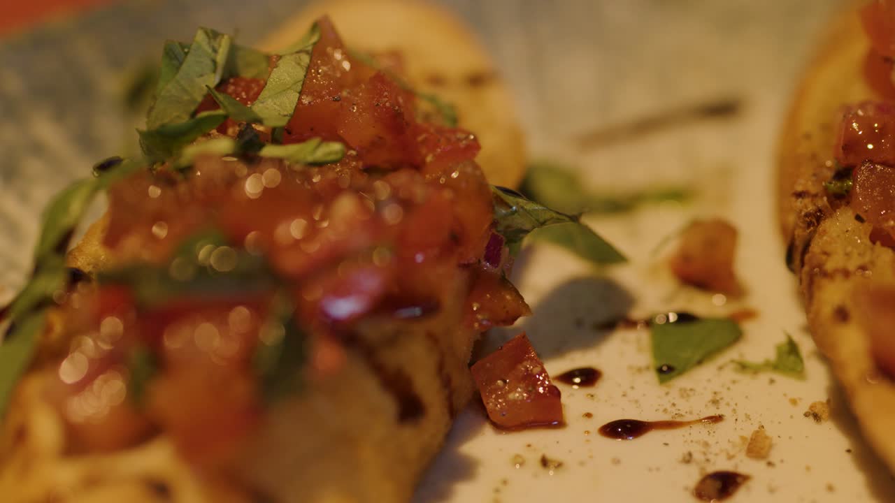 Close-up of hand picking up bruschetta from plate, shallow depth, warm ambient lighting