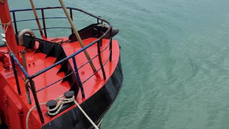 Front-of-a-static-red-tugboat-marine-vessel-with-ripples-in-the-sea-from-a-gentle-breeze-in-Raglan,-New-Zealand