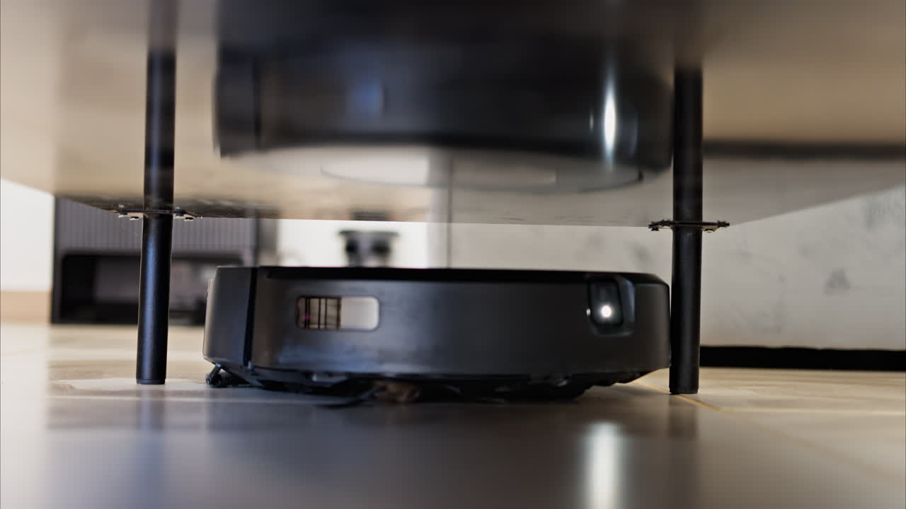 Close up of a small, black robot vacuum cleaning under surfaces in the house