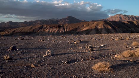 Arid-ground-with-dry-shrubs-in-Mojave-Desert,-California-with-Sierra-Nevada-in-the-distance,-Aerial-flyover-low-slow-shot