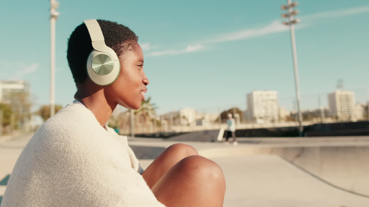 Giovane donna afroamericana che ascolta musica con le cuffie in un parco urbano