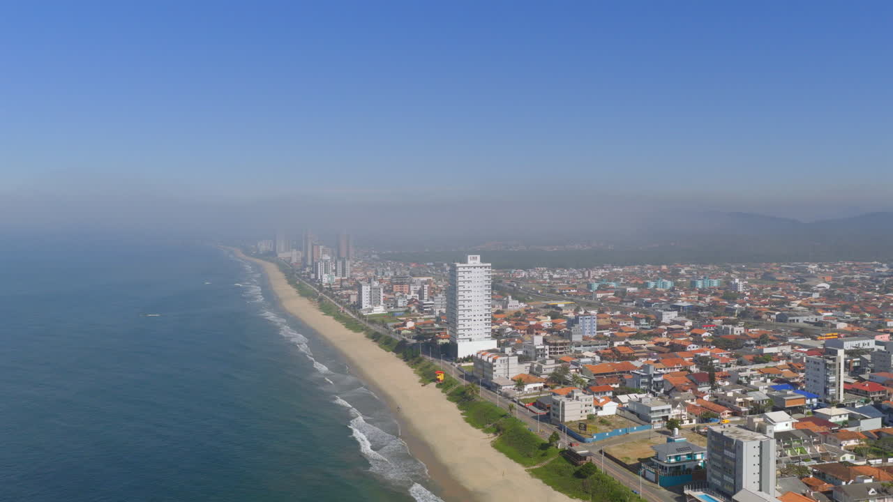 Upward panorama drone fly of coastline with sandy beach and local buildings lined along oceanfront, Barra Velha, Santa Catarina, Brazil