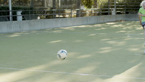 focused senior man running and kicking ball while playing football with friends in a stadium