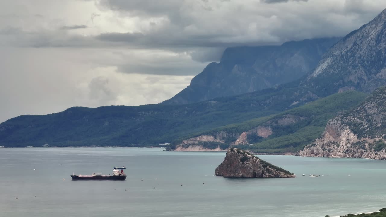 구름이 가득한 하늘 아래 배와 산이 있는 해안 풍경