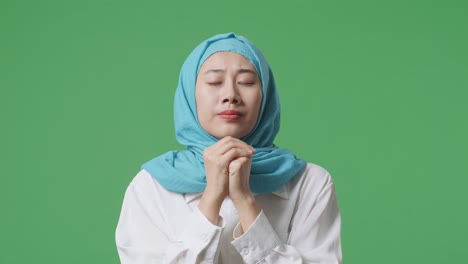 close up of asian muslim woman praying for something while standing in the green screen background studio