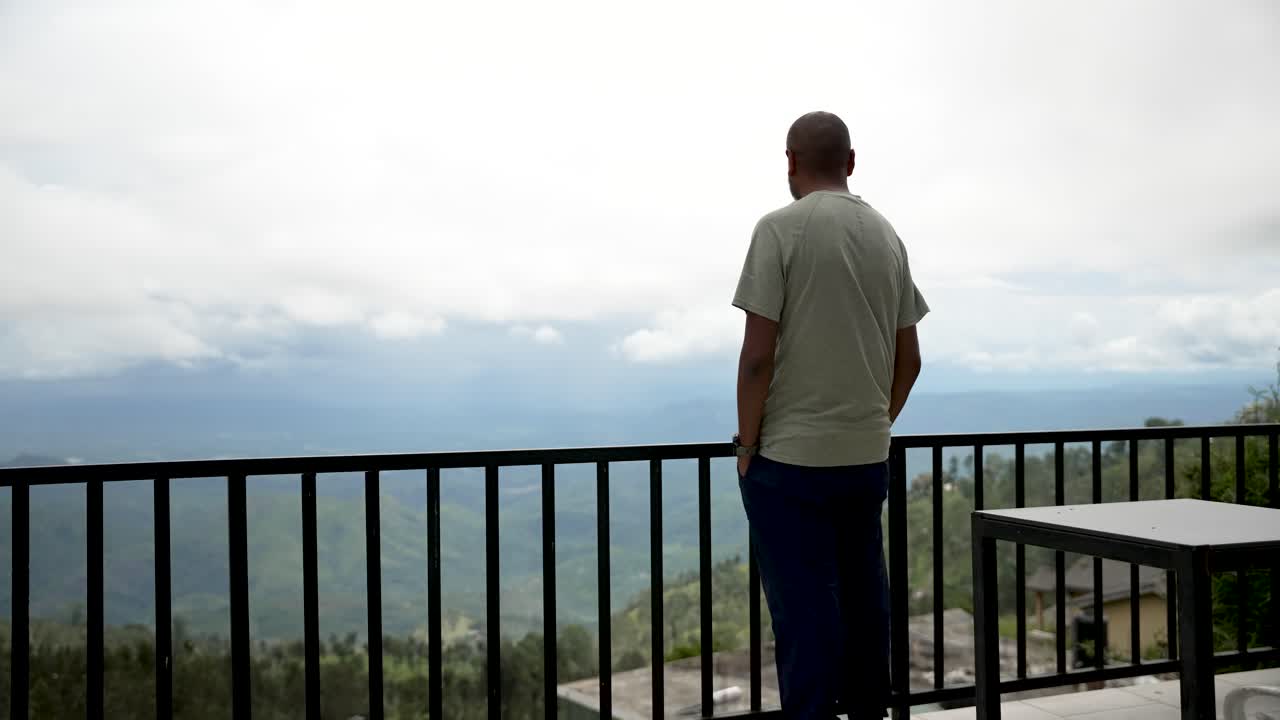 A man enjoys a peaceful moment on a balcony, overlooking a gorgeous valley view.