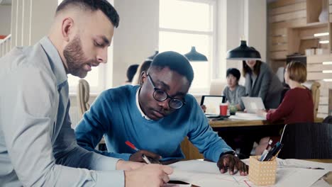 two multi ethnic colleagues work on architecture project in trendy loft office space, teamwork in the background 4k