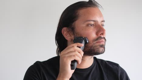 latino man trimming beard and mustache with electric razor, pre-shave oil