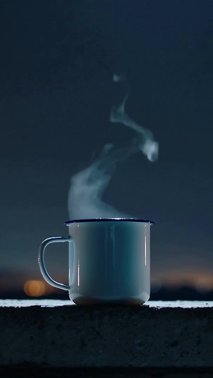 Video verticale: Tazza bianca con bordo scuro che rilascia vapore dal calore, su una sporgenza di cemento di notte