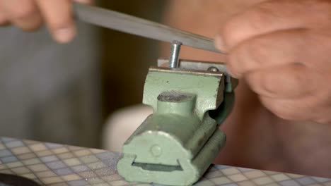 close-up, the old man handles the file clamped in the vise bolt
