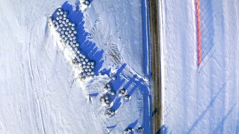 hay balls on field by road in winter, aerial view