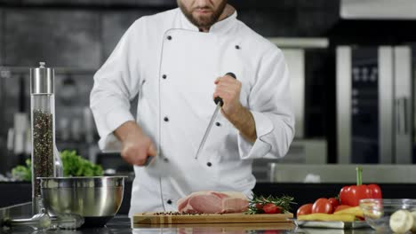 Chef-preparing-to-cook-meat-at-kitchen.-Closeup-chef-hands-sharpening-knife.