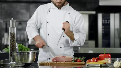 el chef se prepara para cocinar carne en la cocina. el chef de primer plano tiene las manos afilando el cuchillo.