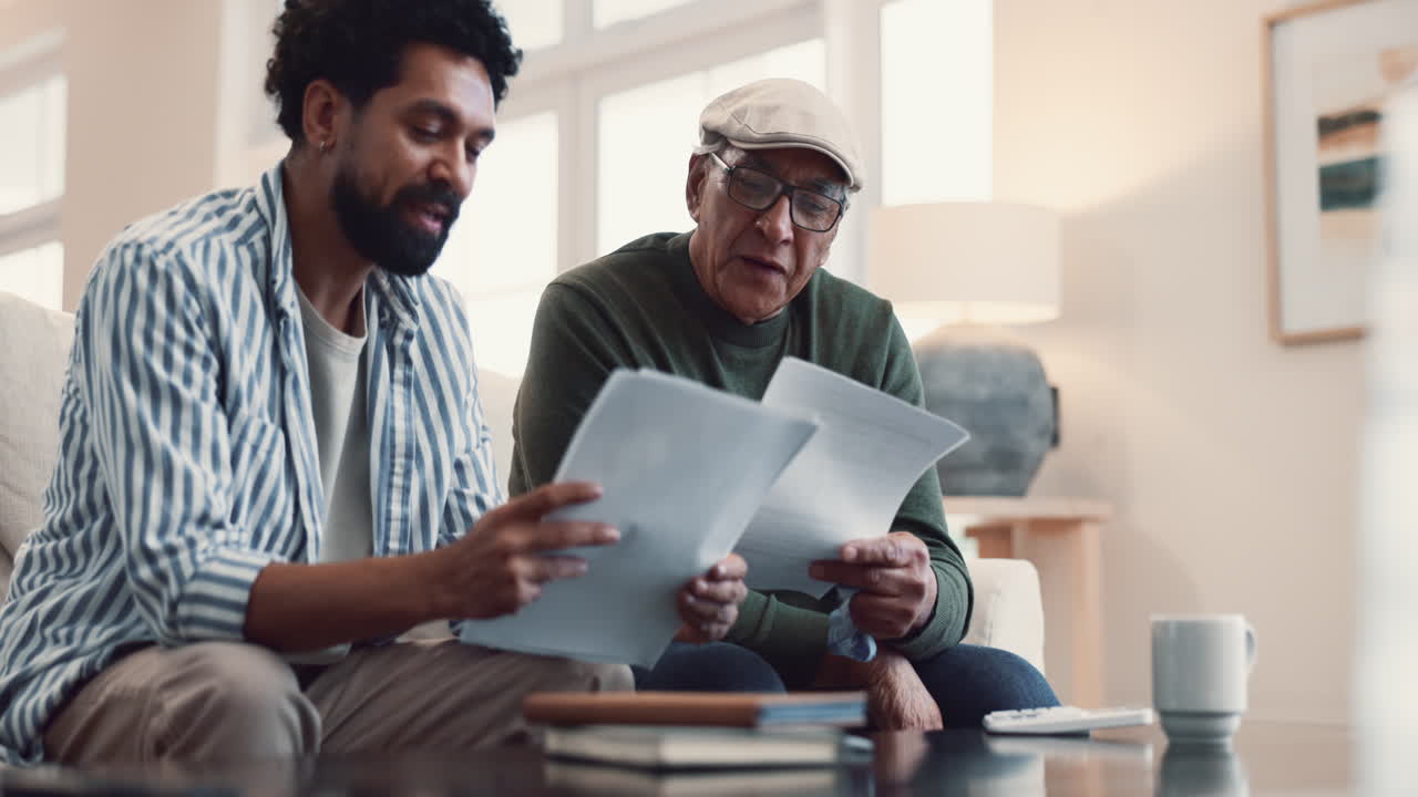 A father and son sit on a couch looking over documents and talking
