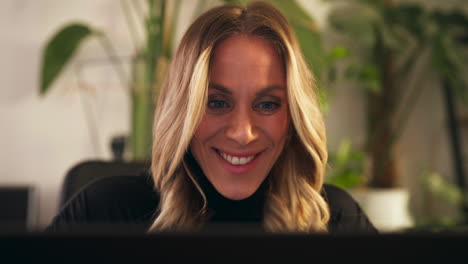 a woman working from her home office, smiling as she looks at her screen - close up