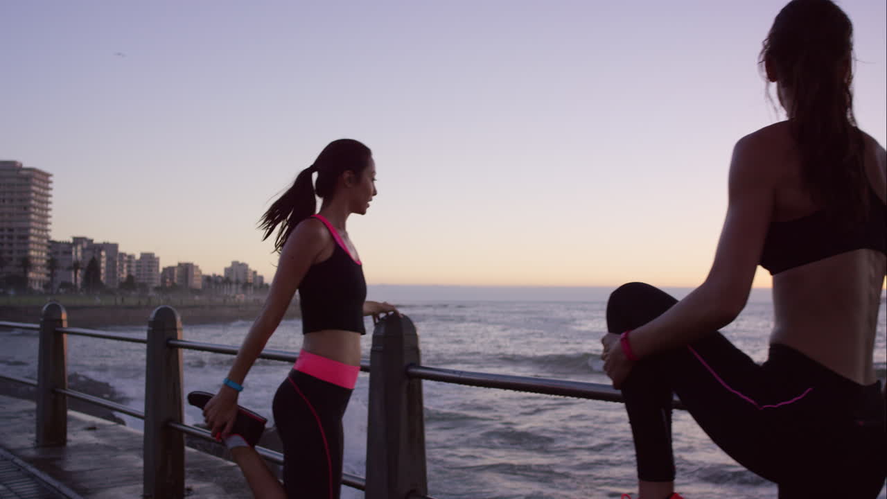 dos amigos atléticos estirándose antes de una carrera en el paseo marítimo al atardecer