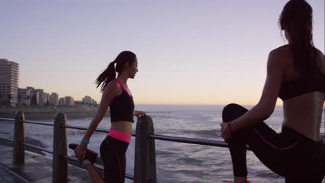 two athletic friends stretching before a run on promenade at sunset