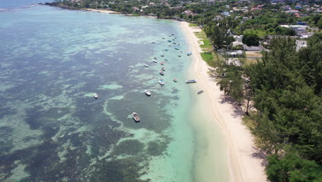 drone slowly flies towards a beautiful beach and clear water with lots of small fishing boats near the town of albion on the island of mauritius