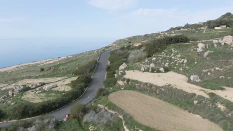 white racing car driving fast on the curvy road track uphill under the blue sky - aerial shot