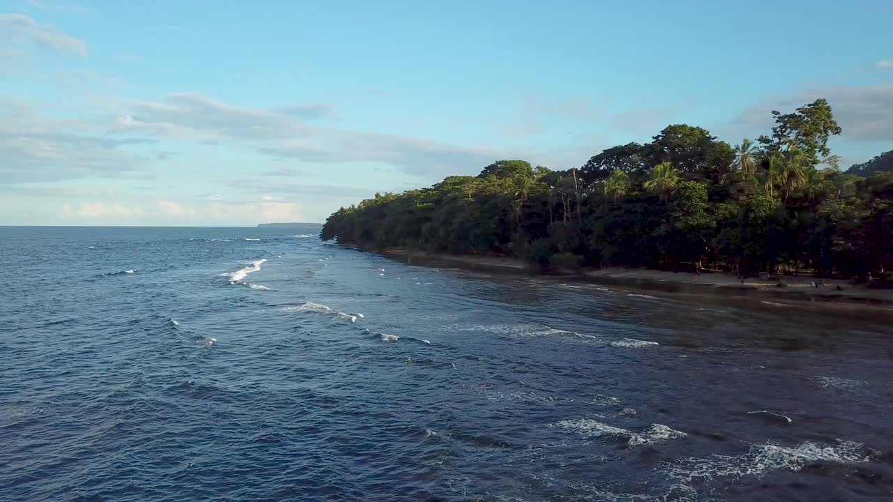 Drone che vola sopra le onde e l'acqua verso la terraferma nel bellissimo cielo blu di Puerto Viejo de Talamanca in Costa Rica.