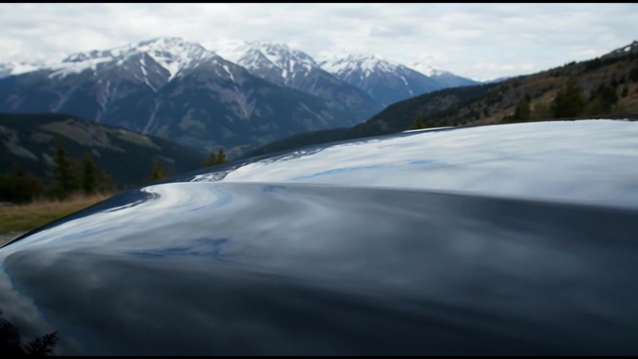 Primo piano del cofano dell'auto che riflette un paesaggio montano