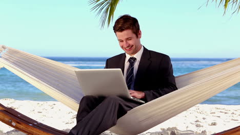 hombre de negocios escribiendo en su portátil en una hamaca y sonriendo