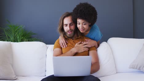 Mixed-race-couple-looking-at-laptop-and-embracing-in-living-room